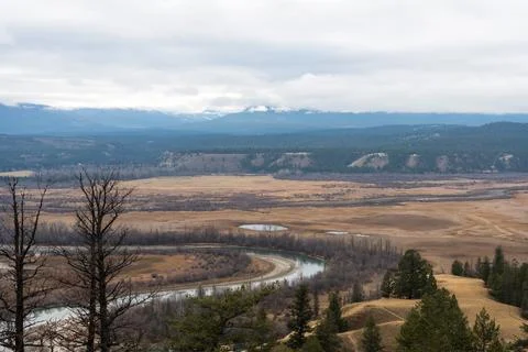 Expansive landscape features a winding river, field, and distant mountains. Stock Photos