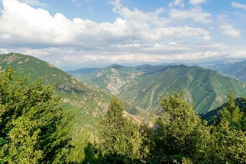 Expansive mountain range covered in lush green trees under a cloudy sky Stock Photos