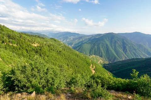 Expansive mountain range covered in lush green trees under a cloudy sky Stock Photos