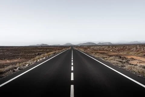 Expansive road stretches through arid landscape under a clear sky Stock Photos