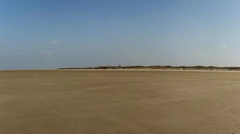 Expansive Sandy Beach with Remote Lighthouse beyond Rolling Dunes under Vas.. Stock Photos