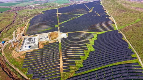 Expansive solar panel array capturing sunlight across green hills under a clear Stock Footage 331267755