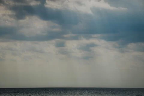 Expansive view of calm ocean waters under a cloudy sky with rays of sunligh.. Stock Photos
