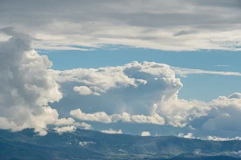 Expansive white cloudscape, varying cloud sizes, mountain range backdrop, sof Stockfoto's