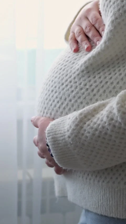 Expectant mother affectionately caressing her pregnant belly, standing by the Stock Footage 341284285