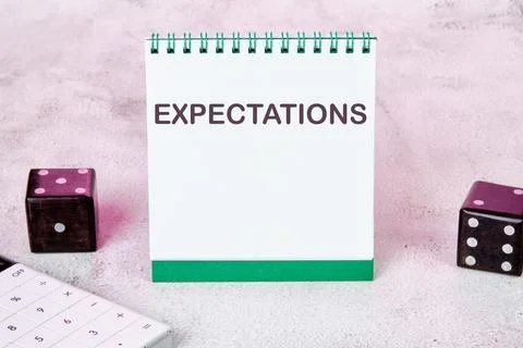 EXPECTATIONS text on a white notepad sheet next to dice on an abstract back.. Stock Photos