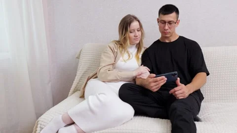 Expecting couple browsing smartphone at home Stock Footage 303877573