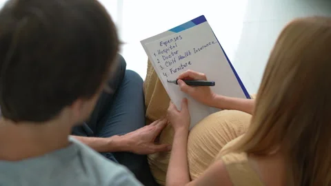 Expecting couple sitting on the couch discussing future baby expenses. Pregnant Stock Footage 318603824