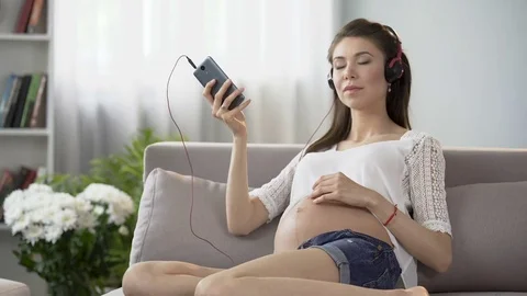 Expecting lady listening to relaxing music on cellphone and rubbing belly Stock Footage
