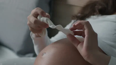 Expecting mother checks small socks and applies them to pregnant belly at home Stock Footage 169525778
