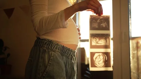 Expecting mother gently cradling her pregnant belly while holding a sonogram Stock Footage 330195468