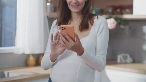 An Expecting Mother is Using Her Smartphone While in a Modern Kitchen with a Stock Footage 316035403