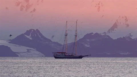 Expedition sailing ship beneath Antarctic mountains at sunset Видео 343121598