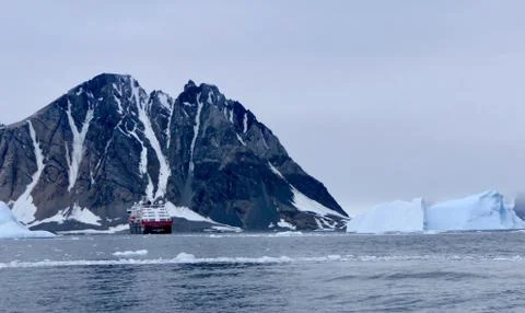 Expedition ship between icebergs in antarctic sea with mountain, Antarctica Stock Photos