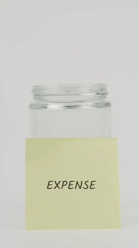 Expense text or word on yellow sticky note attached to glass jar with hand Stock Footage 311729531