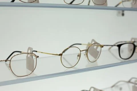 Expensive glasses with thin frames on glass shelf at optical store. Premium.. Stock Photos