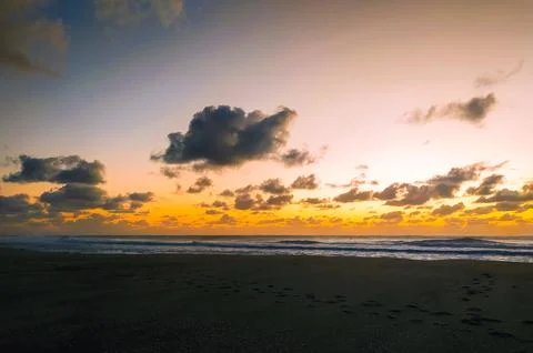 Experience tranquility with this stunning sunset over a dark sandy beach. Foo Stock Photos