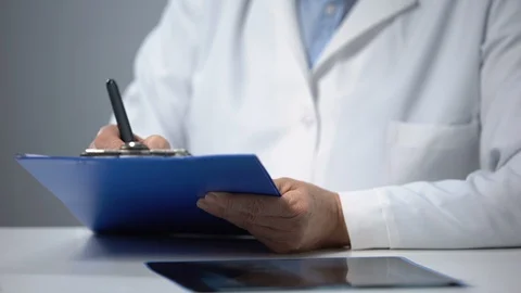 Experienced aged physician writing down medical records and consulting patient 動画素材 119288349
