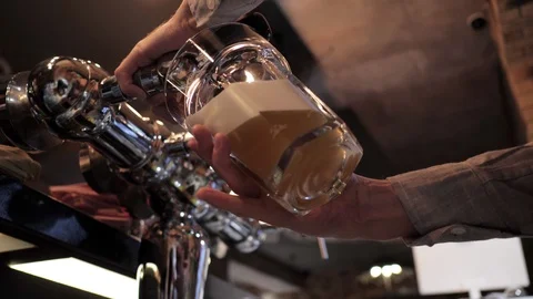 Experienced bartender pours yellow foaming beer into goblet Stock Footage 108311198