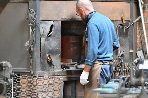 An experienced blacksmith works with open fire. A blacksmith extinguishes a f Stock Photos