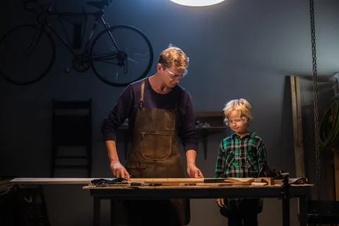 An experienced carpenter shows the work of various tools to his son in the Stock Photos