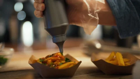 An experienced chef carefully pours sauce over freshly cooked French fries w Stock Footage 323727185