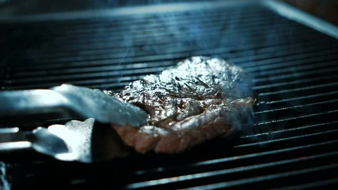 Experienced cook is frying beef slice on grill in kitchen of restaurant. Stock Footage 88572121