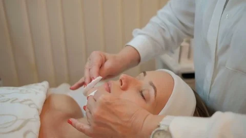 Experienced cosmetologist cleanses face of client with cotton swabs in clinic. Video stock 82737340