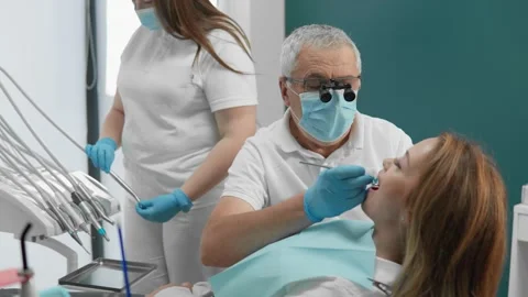 Experienced dentist in protective mask and magnifying glasses performing dental 库存影片 341036252