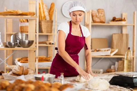 Experienced female baker preparing raw dough on kitchen table in bakery Stock Photos