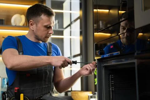 Experienced foreman fixes oven using screwdriver in kitchen Stock Photos