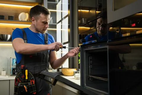 Experienced foreman fixes oven using screwdriver in kitchen Stock Photos