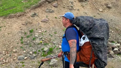 Experienced hiker carrying a large backpack along a rugged mountain trail Vidéo 338005102