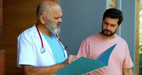 Experienced Indian doctor discusses case with patient in clinic porch Stock Footage 342829891