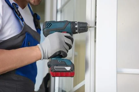 Experienced installer in uniform automatic screwdriver and repairs plastic door Stock Photos