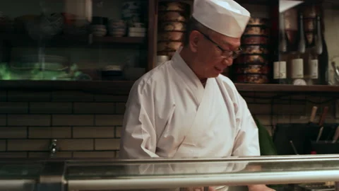 Experienced Itamae sushi chef talking with two customers while they eat in small Stock Footage 199460452