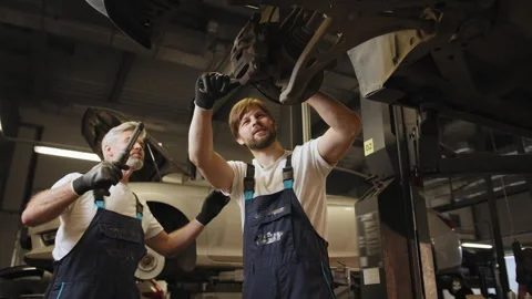 Experienced mechanic staring at the car underside vehicle on a lift in service Stock Footage 243094307