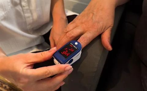 Experienced physician attaching clip of pulse oximeter to male finger Stock Photos