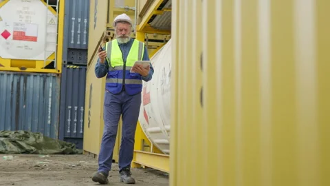 Experienced port worker in a hard hat uses a digital tablet for inventory Stock Footage 346078699