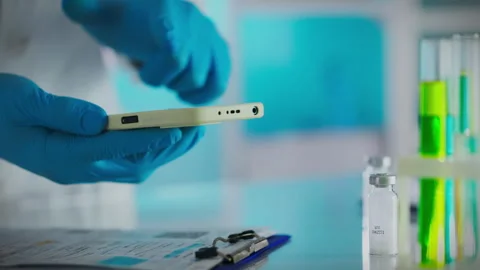 Experienced scientist in blue gloves working efficiently with modern smartph Stock Footage 265080142