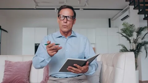 Experienced senior man talks and conducts online client counseling while sitting Stock Footage 217976737