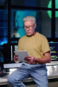 Experienced software developer with tablet sitting on desk against computers Stock Photos