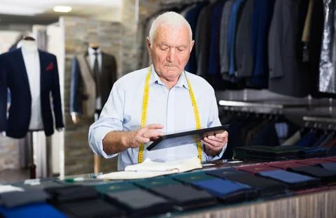 Experienced tailor looks at a pattern on a tablet screen in sewing atelier Stock Photos