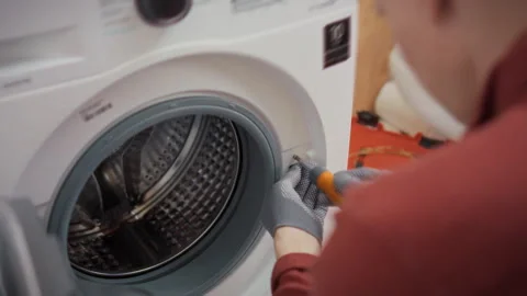 An experienced technician in work uniform unscrews bolts from a washing mach Stock Footage 346391316