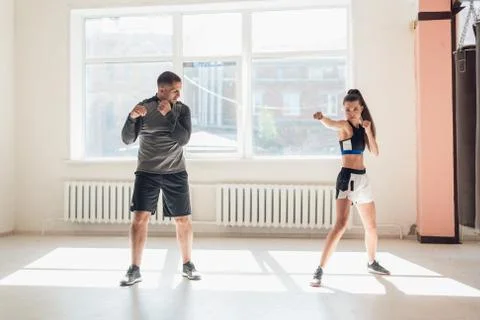 An experienced trainer puts the technique of blows to a young girl in the boxing Stock Photos