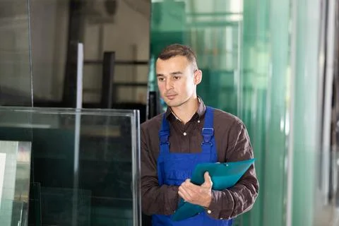 Experienced worker checks the quality of made window glass in an industrial Foto stock