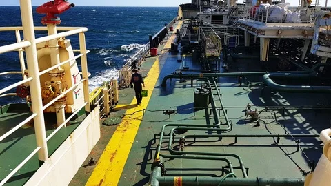 Experienced worker in jumpsuit walks along oil tanker deck Stock Footage 113800860