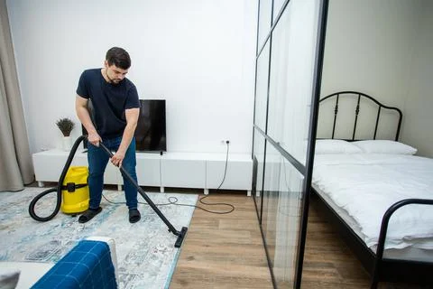 An experienced young guy cleans the floor with a professional vacuum cleaner Stock Photos