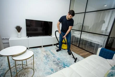 An experienced young guy cleans the floor with a professional vacuum cleaner Stock Photos