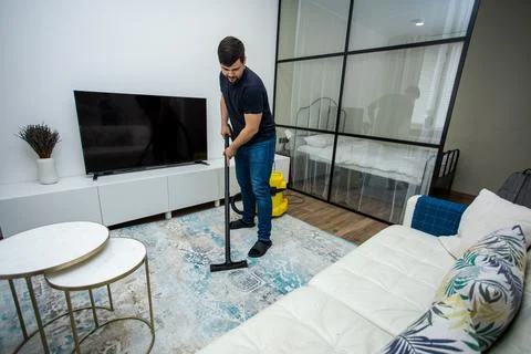 An experienced young guy cleans the floor with a professional vacuum cleaner Stock Photos